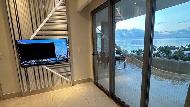 Et moderne hotelværelse med stort fjernsyn, seng, et tæppe med et mønster og en balkon med udsigt over havet.