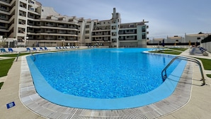 A swimming pool surrounded by a poolside area with lounge chairs, a pool deck, and a multi-story building in the background. - Albufeira Skylight 3 With Pool by Homing (Albufeira)