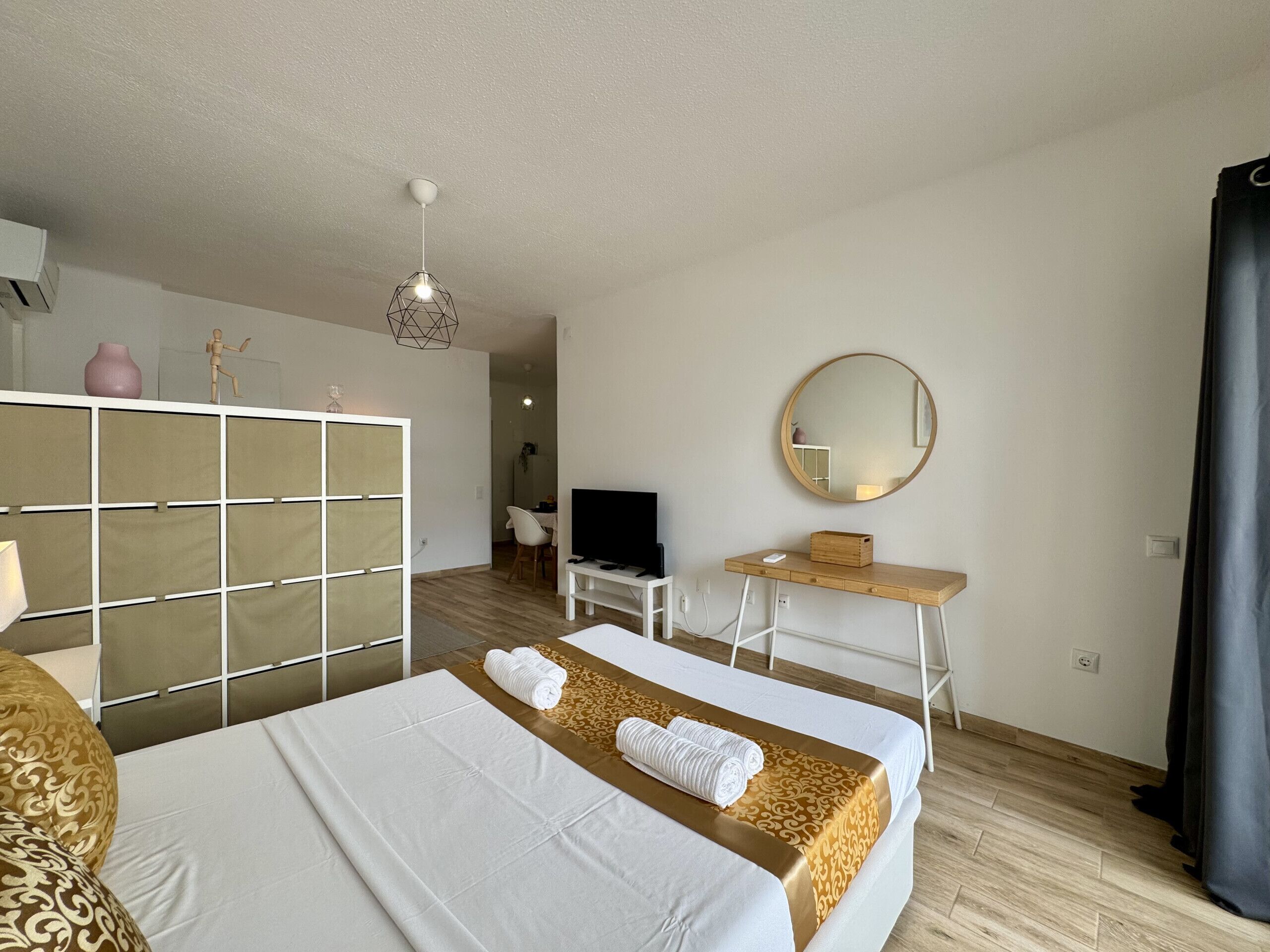 Una habitación de hotel con cama, escritorio, televisor, espejo y armario.