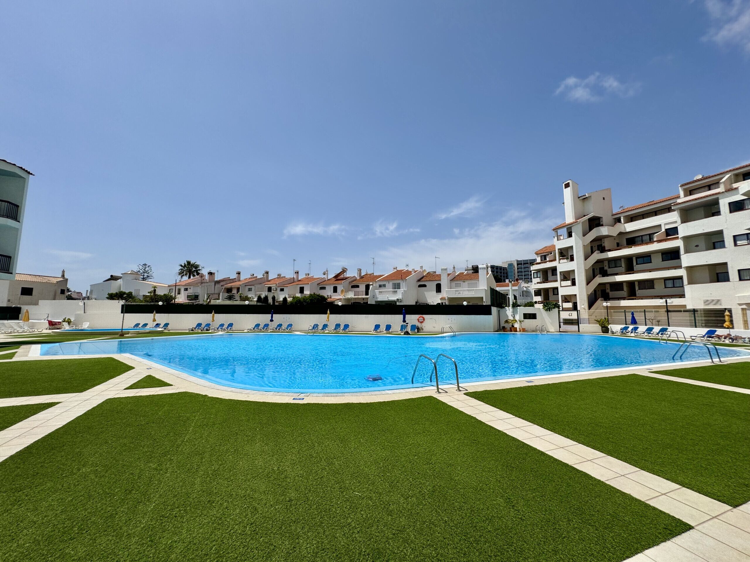 A swimming pool surrounded by artificial grass, with a view of residential buildings in the background.