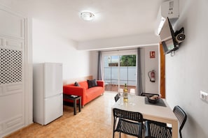 A compact kitchen with a refrigerator, a dining area with a table and chairs, a red sofa, and a window with a view of the outside. - Vacation Home 'My Little Bungalow 49' with Mountain View, Wi-Fi & Air Conditioning (Palm-Mar)
