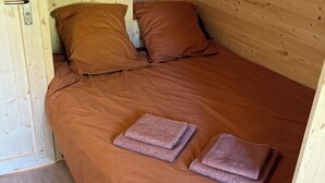 A wooden room with a bed, pillows, a nightstand, a lamp, and a small table. - Quiet cabin in the Fontainebleau forest (Oncy-sur-École)