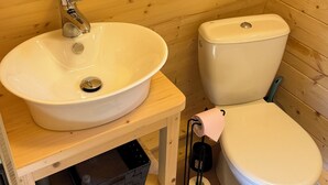 A wooden cabin bathroom with a sink, toilet, and a shelf with a trash can. - Quiet cabin in the Fontainebleau forest (Oncy-sur-École)