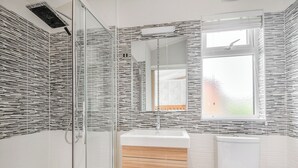 A modern bathroom with a glass shower enclosure, a wooden vanity, and a toilet.
