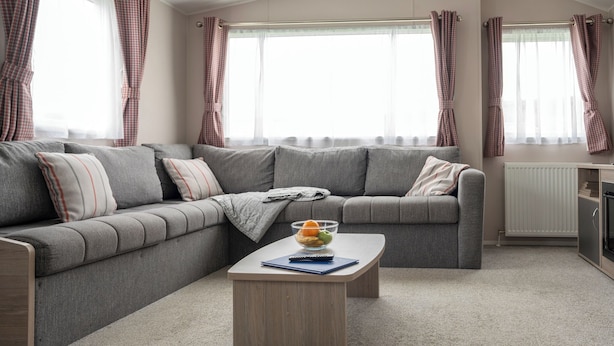 Een moderne woonkamer met een grijze hoekbank, een houten salontafel en een schaal met fruit.