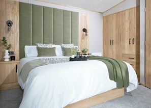 Une chambre avec un grand lit, une armoire en bois et une tête de lit recouverte d’un tissu vert.