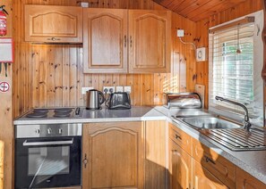 A wooden cabin kitchen with a stove, oven, sink, and cabinets.