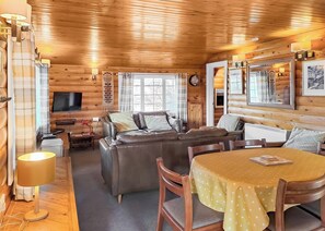 L’intérieur d’une cabane en rondins, avec un canapé, une table à manger et un téléviseur.