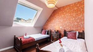 Une chambre avec deux lits, une lucarne, un mur décoré d’un motif et une table de chevet avec une lampe.