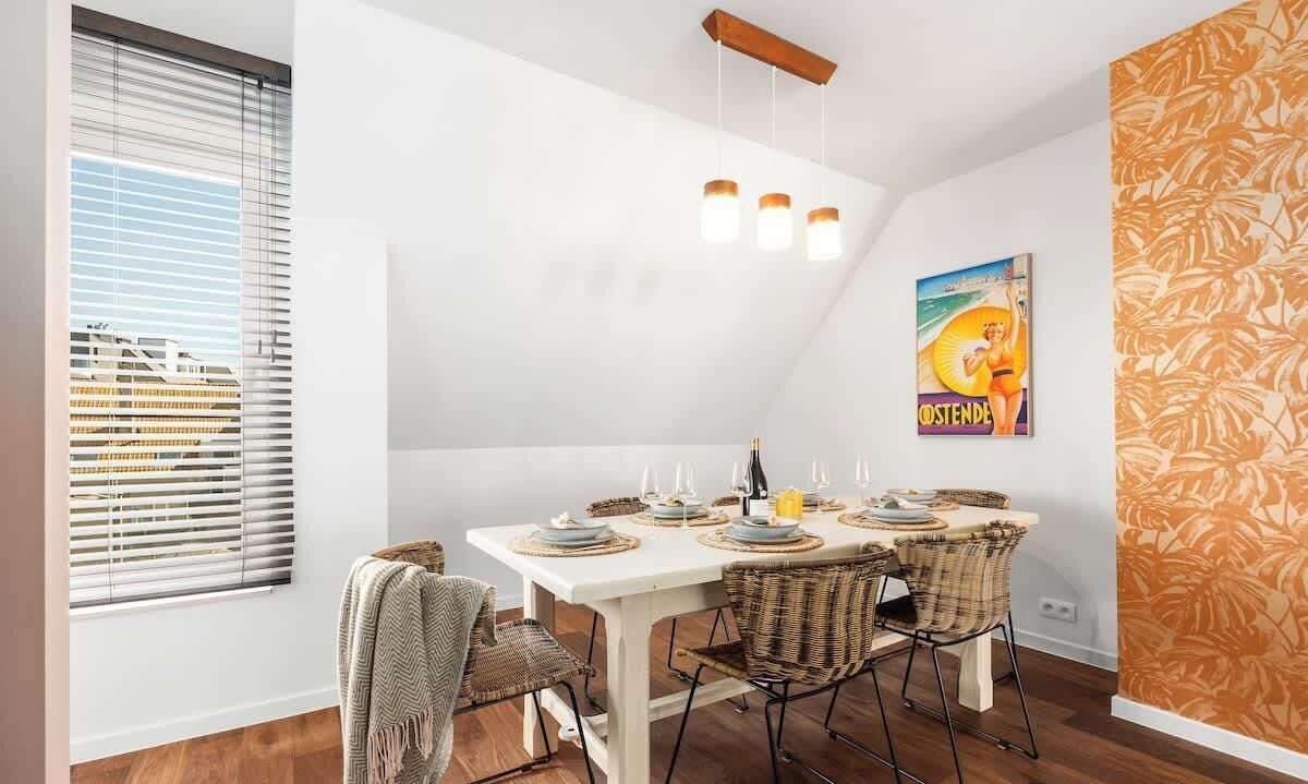 A dining area with a white table set for four, wicker chairs, and a ceiling light fixture.