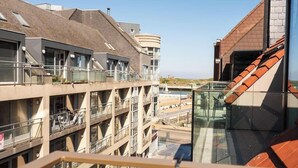 Un immeuble à plusieurs étages doté de balcons, d’une cage d’ascenseur en verre et offrant une vue sur une étendue d’eau.