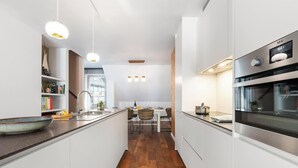 Une cuisine moderne avec des meubles blancs, un plancher en bois et des luminaires suspendus.