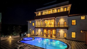Un edificio de dos pisos con piscina, mobiliario exterior y fachada bien iluminada.