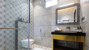 Un baño moderno con cabina de ducha de vidrio, inodoro blanco, tocador negro y dorado, y piso de baldosas con diseño.