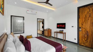Una habitación de hotel moderna con una cama, un televisor, un ventilador de techo y una puerta de madera.