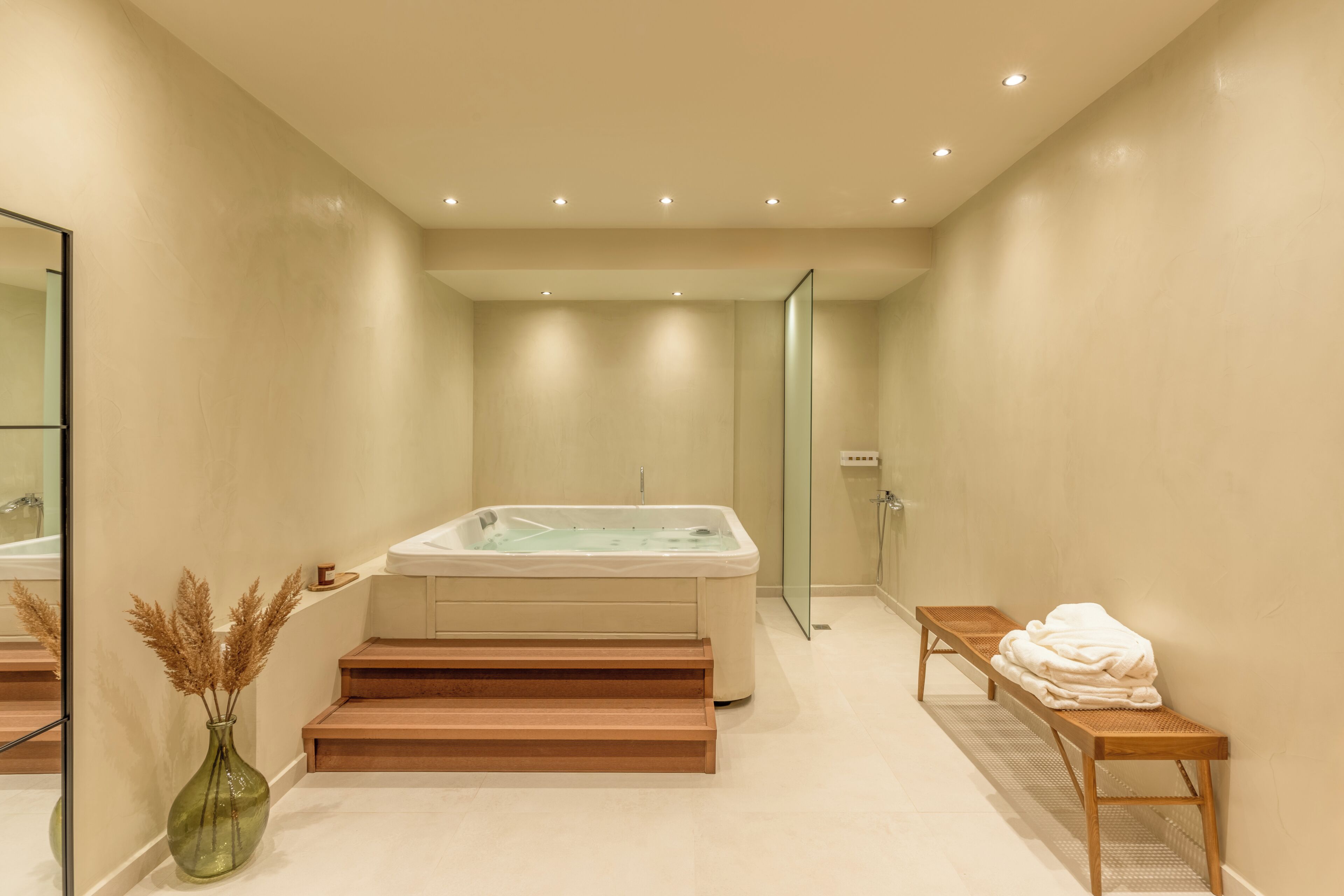 Une salle de bain moderne avec une baignoire, une cabine de douche en verre, un banc en bois et un vase contenant des plantes séchées.