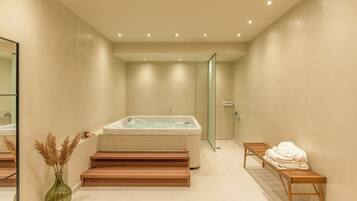 A modern bathroom with a bathtub, a glass shower enclosure, a wooden bench, and a vase with dried plants.