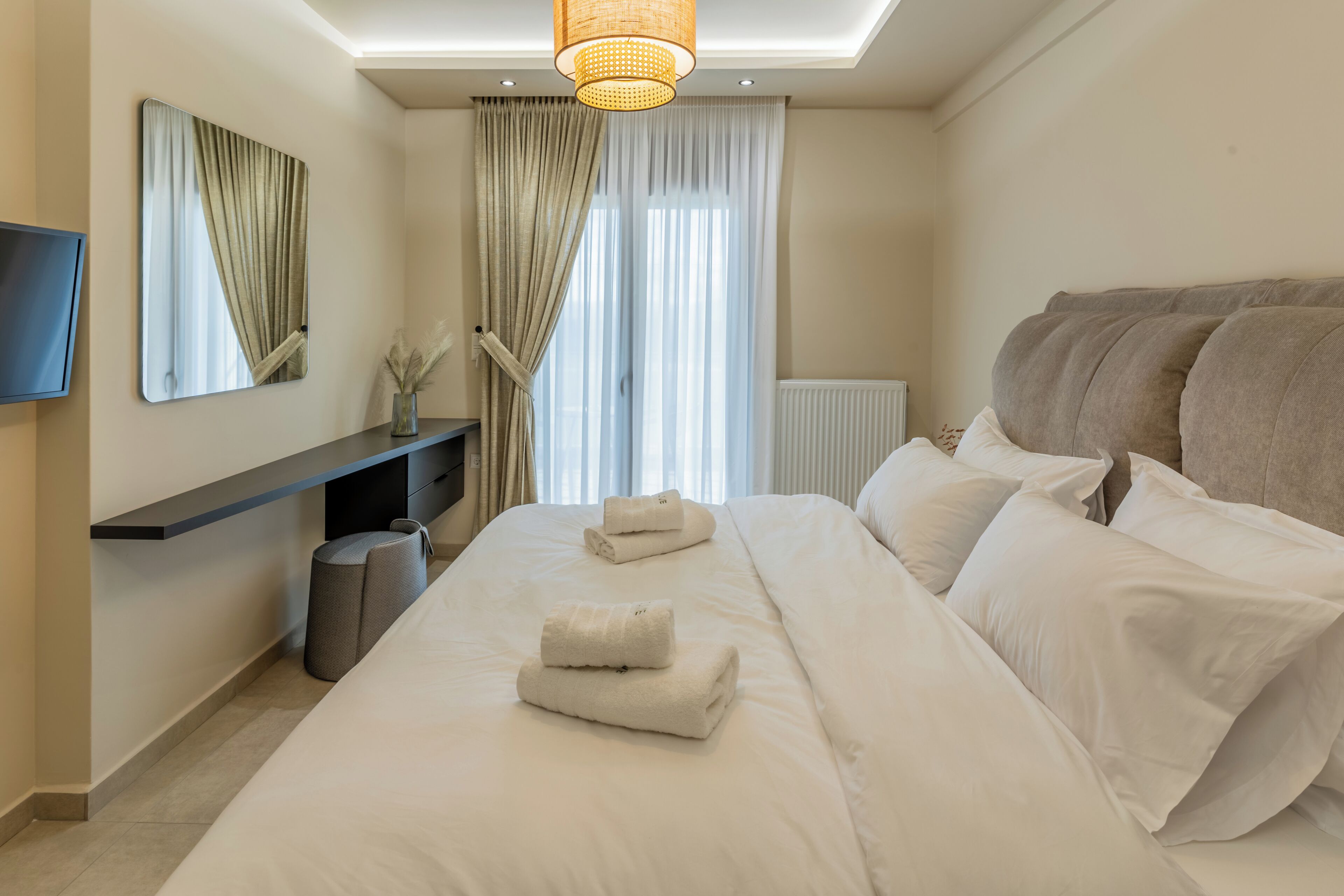 Une chambre d’hôtel moderne dotée d’un grand lit, d’une télévision à écran plat, d’une table de chevet et d’une fenêtre avec des rideaux.
