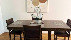 Ein Essbereich mit einem rechteckigen Tisch, vier Stühlen, einer Vase mit weißen Blumen und einem an der Wand hängenden abstrakten Gemälde.