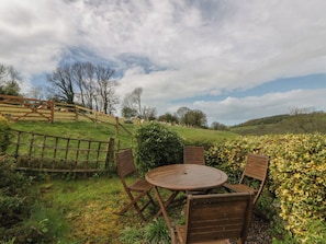 A round wooden table with four chairs, surrounded by greenery and a wooden fence. - Tyn Y Fron (Llanon)