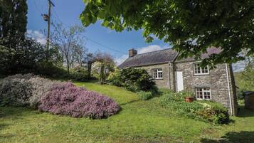 A stone building with a grassy yard, a purple bush, and a clear sky.
