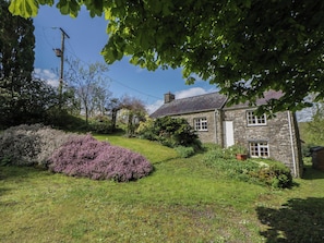 A stone building with a grassy yard, a purple bush, and a clear sky. - Tyn Y Fron (Llanon)