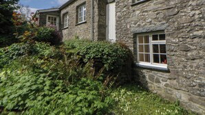 A stone building with multiple windows and a door, surrounded by greenery. - Tyn Y Fron (Llanon)