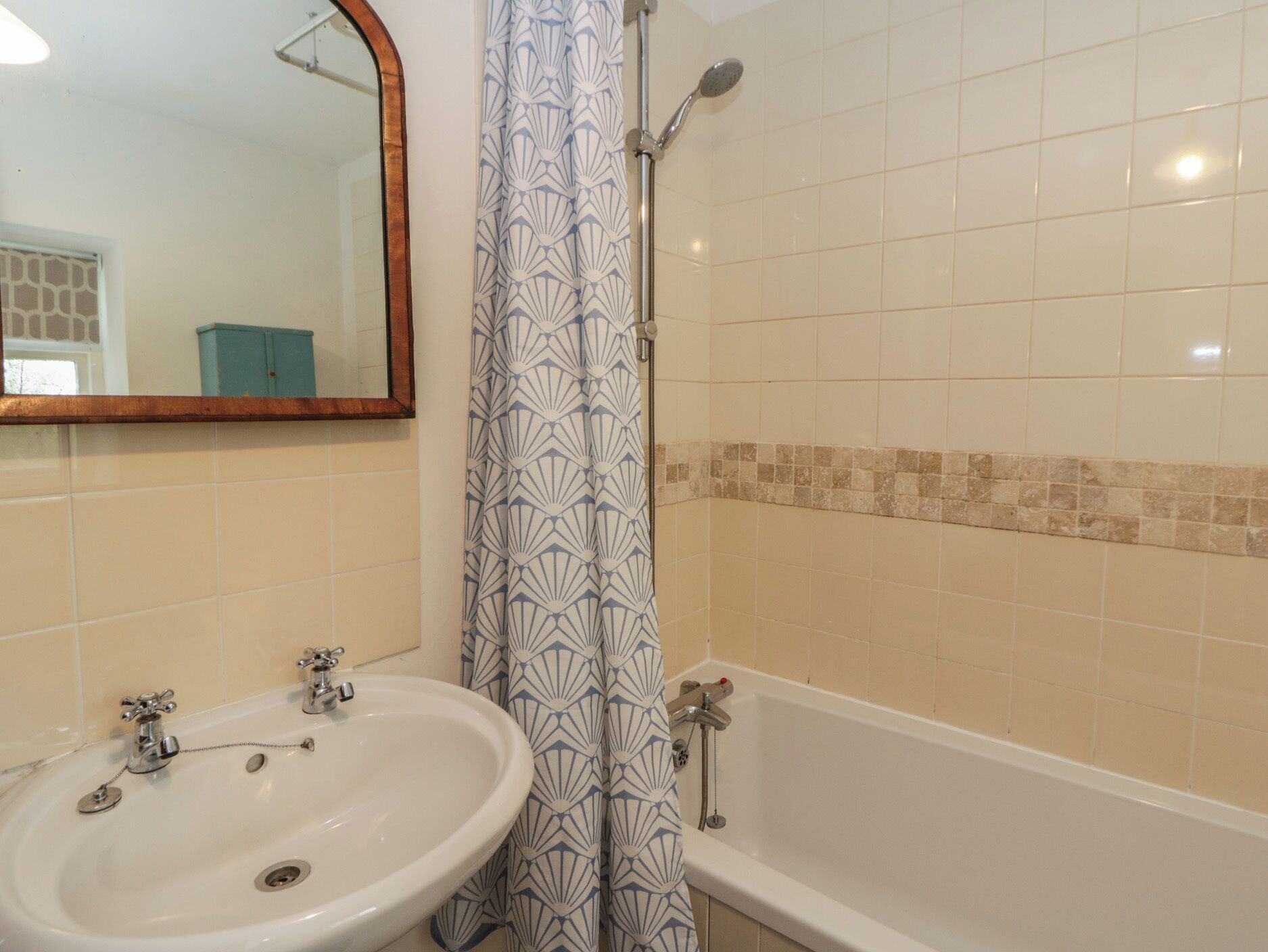 A bathroom with a sink, mirror, shower, and tiled walls.