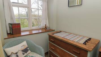 A room with a window, a chair, a wooden dresser, and a small table.