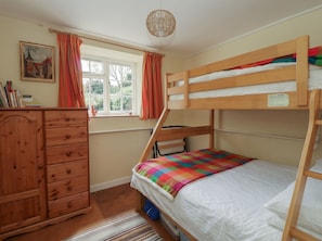 A bunk bed room with a wooden dresser, a window with curtains, and a painting on the wall.
