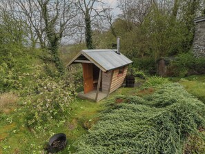 A small wooden cabin with a metal roof, surrounded by lush greenery and a rustic setting.