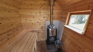 A wooden cabin interior with a wood-burning stove, a window, and a metal bucket.