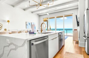 A modern kitchen with a large island, stainless steel appliances, and a view of the ocean. - BRAND NEW, Elevated Pool, Beach Front, Hot Tub, and Elevator - Dune Alright (St. George Island)