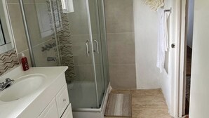 Un baño con cabina de ducha de vidrio, un lavamanos blanco y zona de ducha con azulejos.