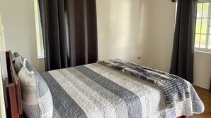 Un dormitorio con cama, cortinas, una ventana y un equipo de aire acondicionado.