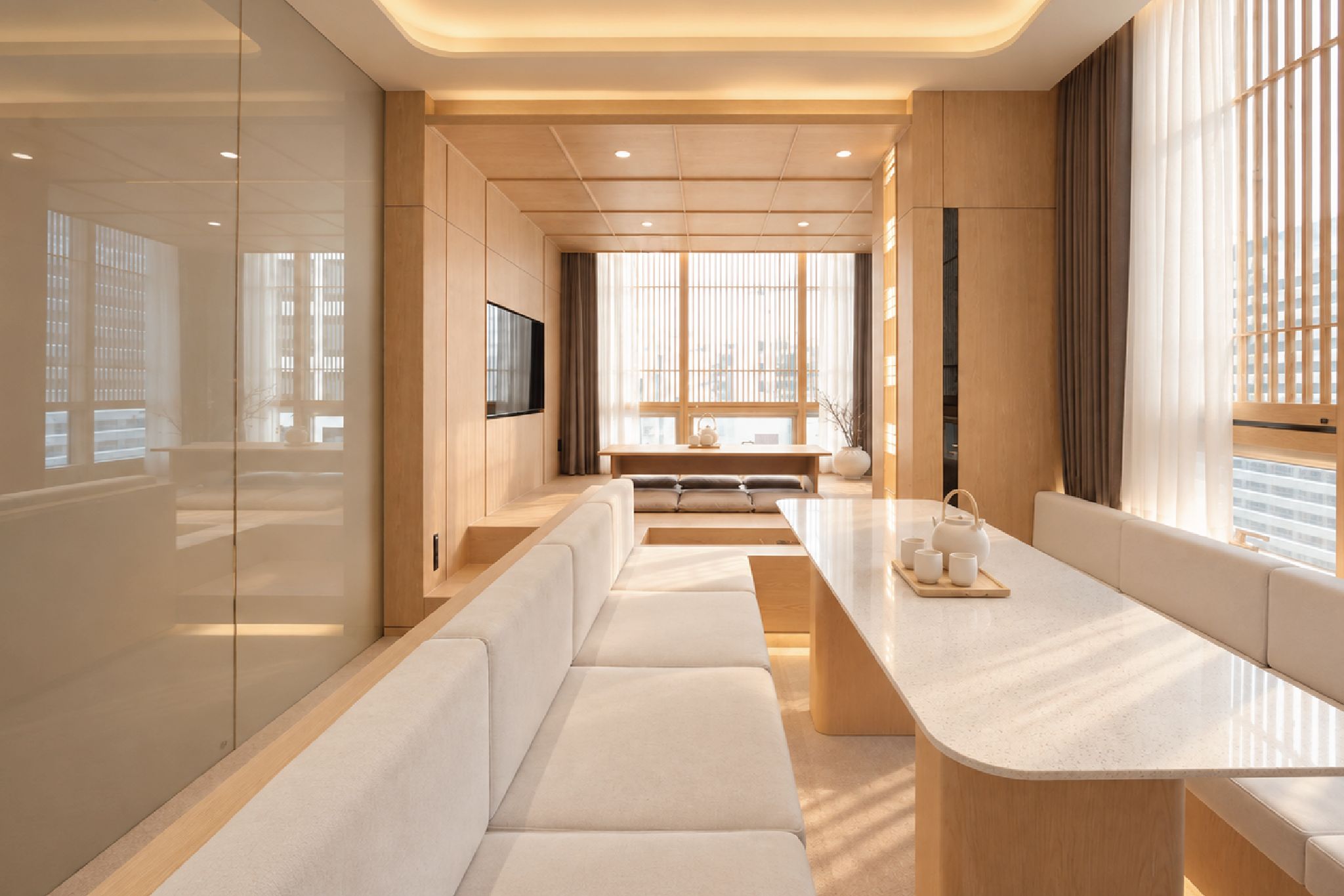 A modern interior with a long bench seating area, a central table, and large windows allowing natural light.