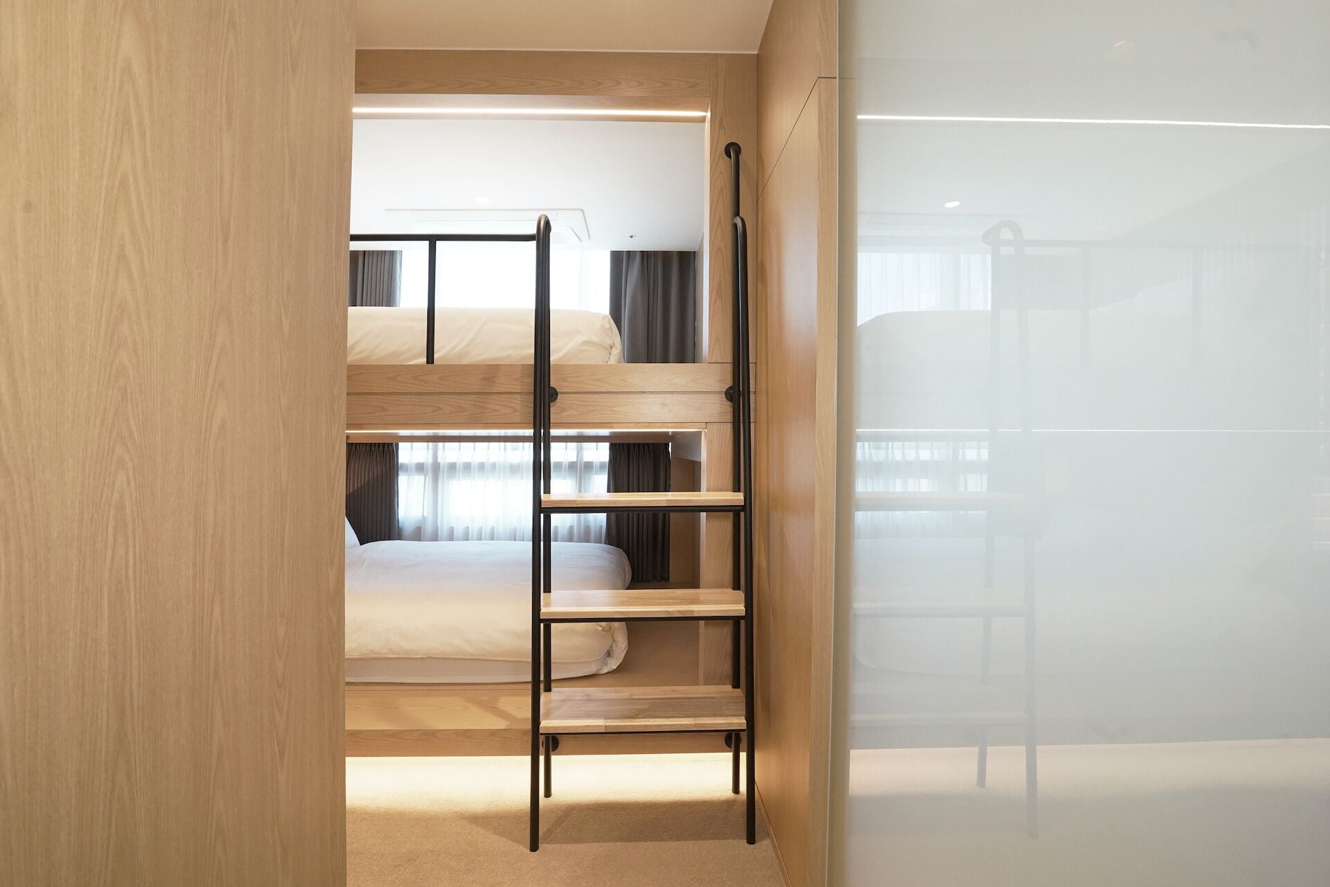 Dormitorio con literas, una escalera, una ventana con cortinas y una pared de madera.