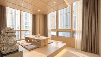 A modern interior with a wooden dining table, a stone sculpture, and large windows with curtains.