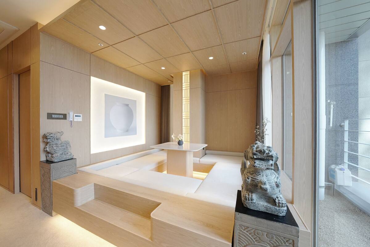 A modern interior with a wooden ceiling, recessed lighting, a central seating area, and decorative sculptures.