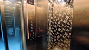 Interior de un ascensor con detalles metálicos, un panel de control con botones numerados y una puerta de vidrio con diseño.