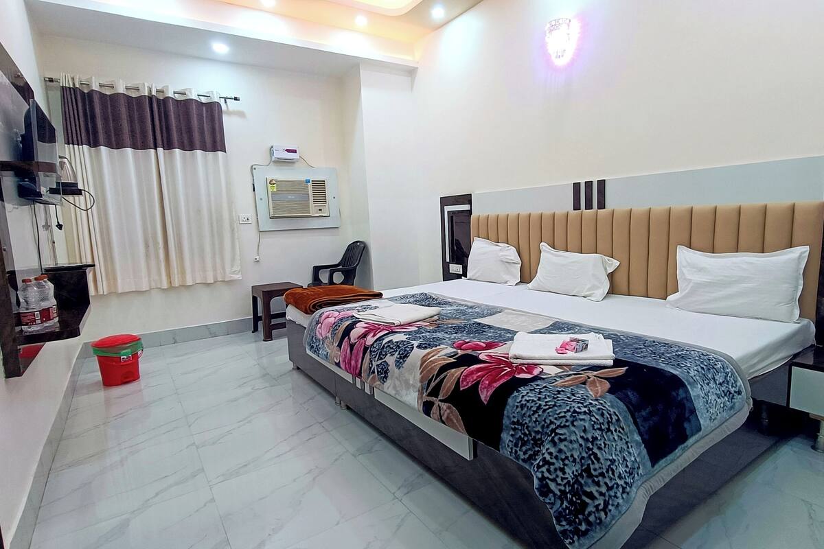 Habitación de hotel con cama, escritorio, silla, televisión, baño y un cubo rojo.