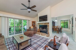 Ein geräumiges Wohnzimmer mit Kamin, Deckenventilator und großem, darüber montiertem Fernseher.