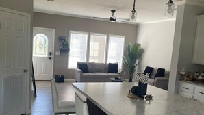 Una cocina moderna con una isla de mármol, muebles blancos e iluminación colgante.