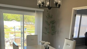 Un comedor con una mesa blanca, cuatro sillas, una lámpara de araña y una planta en maceta.