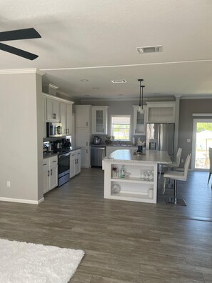 A spacious kitchen with white cabinetry, a central island, and a dining area with chairs. - Perfect 3-bedroom mobile home in nature paradise (Okeechobee)