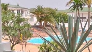 Een balkon met uitzicht op een zwembad, palmbomen en een gebouw op de achtergrond.