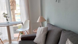 Een moderne woonkamer met een grijze bank, een klein rond tafeltje, een lamp en uitzicht op de omgeving.