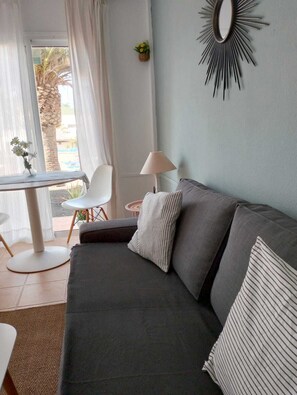 A modern living room with a grey sofa, a small round table, a lamp, and a view of the outdoors. - Apartamento Verdemare, a completely renovated vacation apartment Corralejo (Corralejo)