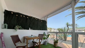 Een balkon met een tafel en stoelen, een decoratieve muur, en uitzicht op een zwembad en palmbomen.