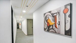 A hallway with a modern art piece on the wall, a door, and a carpeted floor.